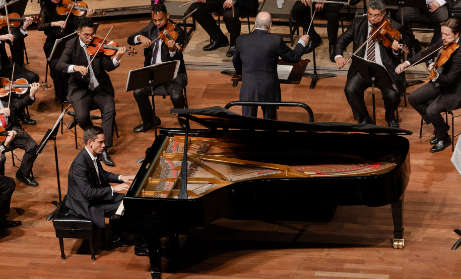pianista sentado em frente ao piano, orquestra ao fundo