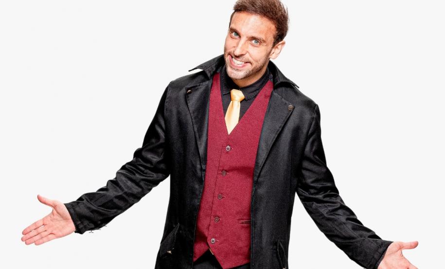 Léo Lins em frente a fundo branco com braços abertos e sorrindo