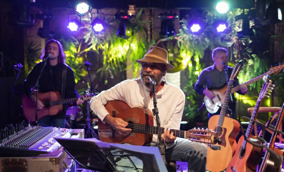 Almir Sater e banda com instrumentos e luzes ao fundo