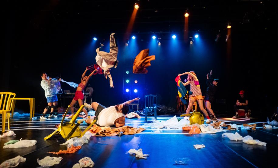 Cena da peça Deriva mostra atores jogando roupas para o ar