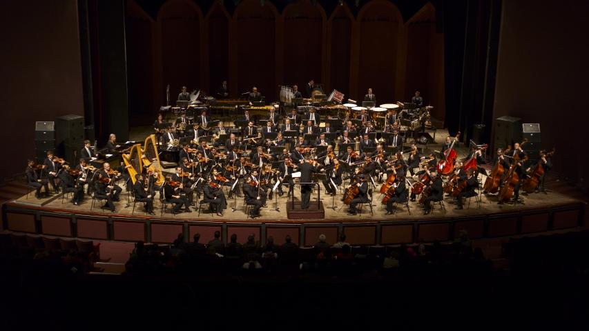 Foto dos músicos da Orquestra tocando seus instrumentos no palco do Guairão